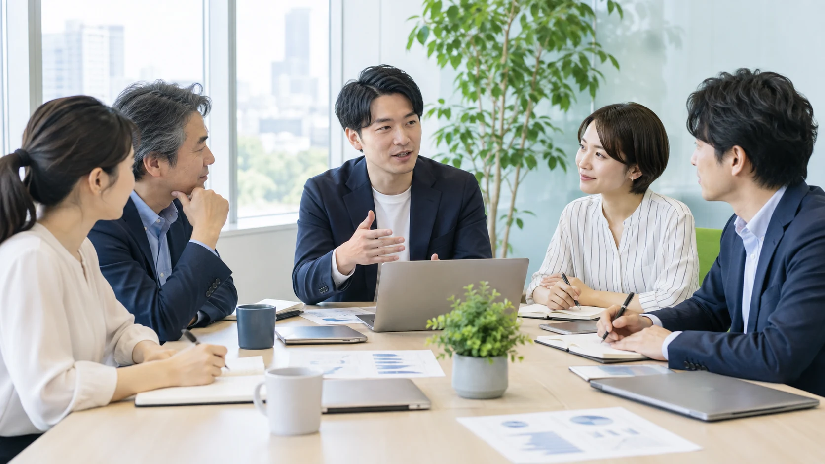 複数の社員がテーブルを囲み、仕事の進め方を話し合う会議のイメージ